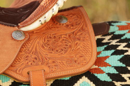Close-up of a brown leather saddle with intricate patterns on a colorful patterned blanket.