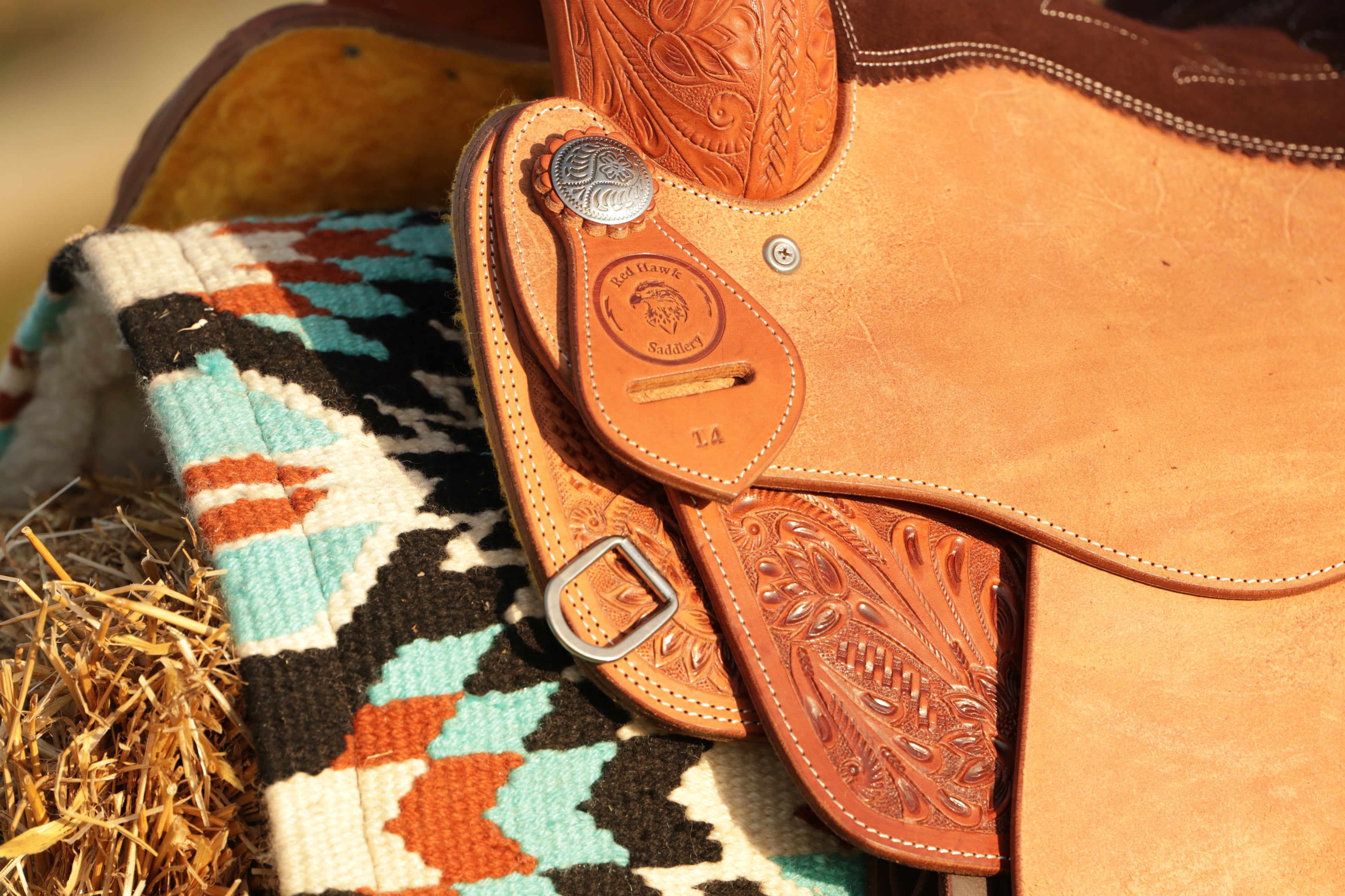 Close-up of a leather saddle with intricate designs on a patterned blanket.