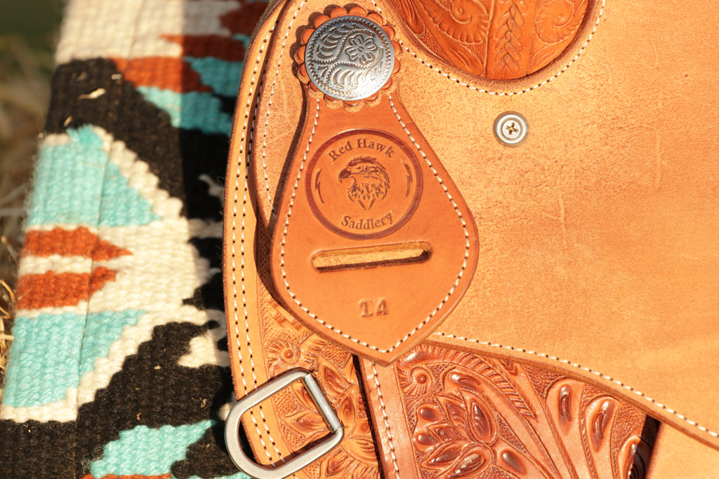 Close-up of a leather saddle with intricate designs and branding against a colorful patterned background.